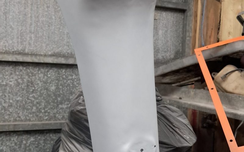 Grey primed motorcycle body panel hanging from a wire in a workshop, ready for painting.