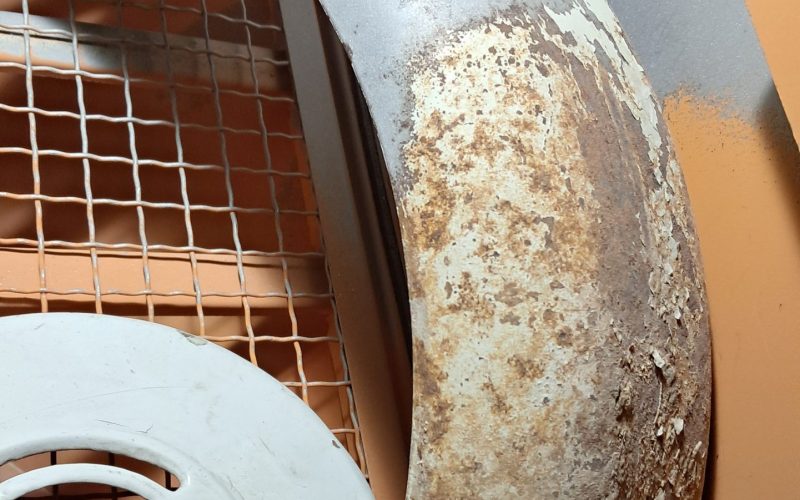 Rusted and partially sanded motorcycle fender inside a blasting booth, showing heavy corrosion and old paint removal.