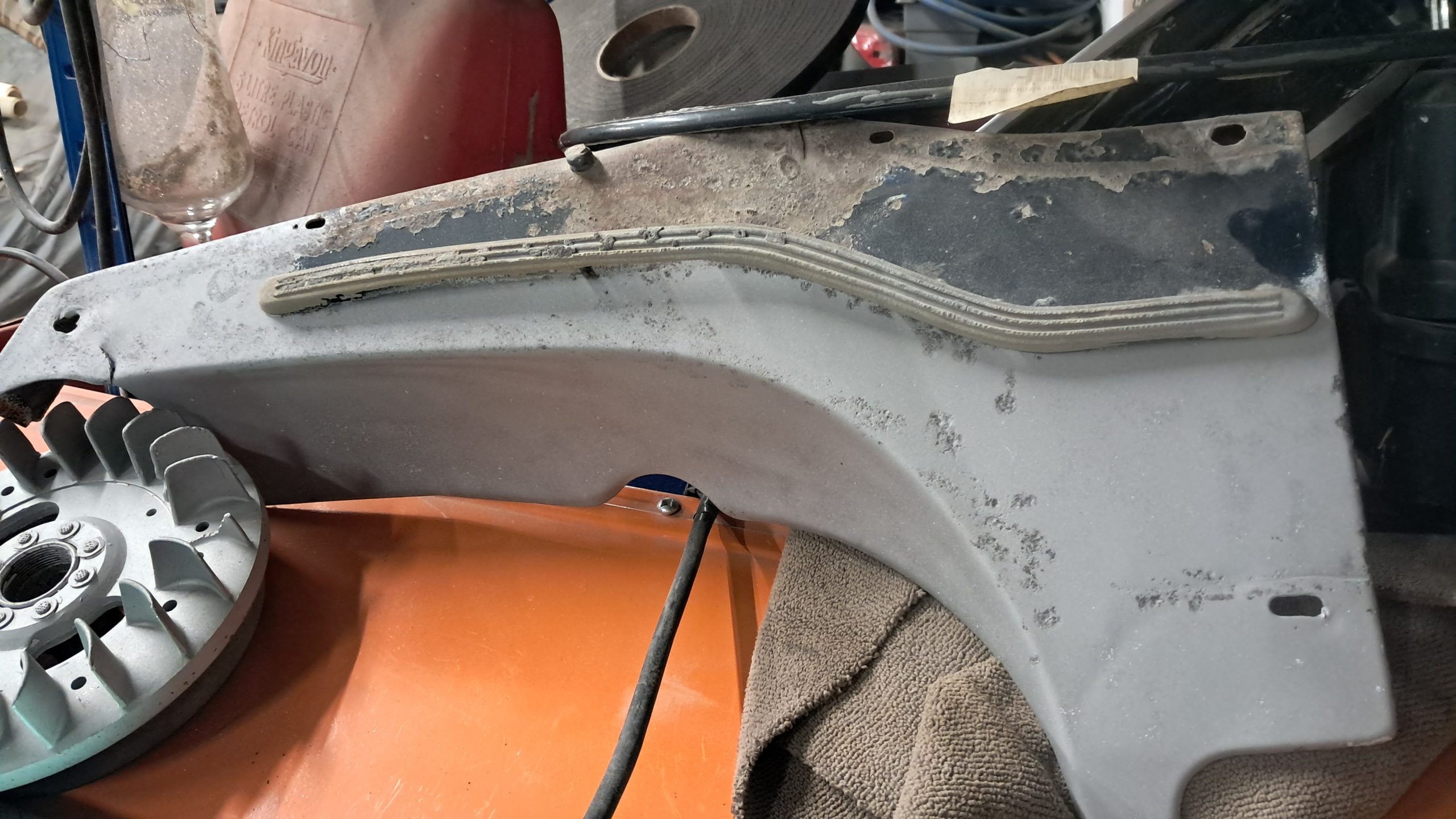 Partially cleaned and sandblasted motorcycle side panel with rubber trim still attached.