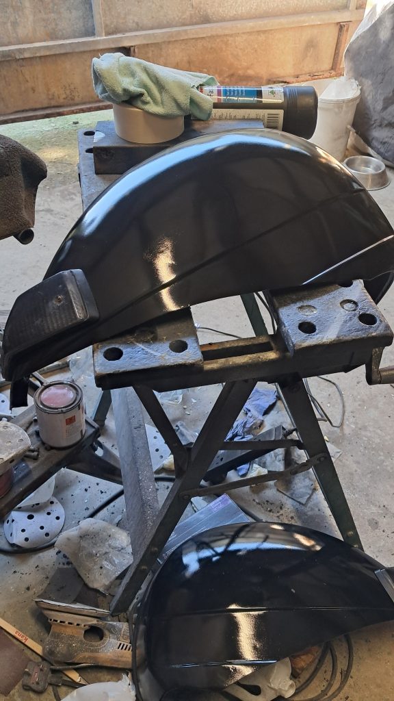 Black painted motorbike mudguard resting on a metal workbench in a workshop, showing a glossy freshly painted finish.