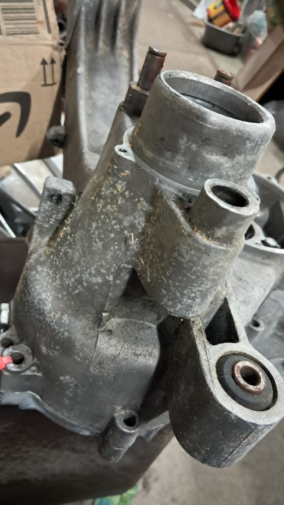 Close-up of an unpainted aluminium engine casing showing corrosion and wear, photographed in a workshop.