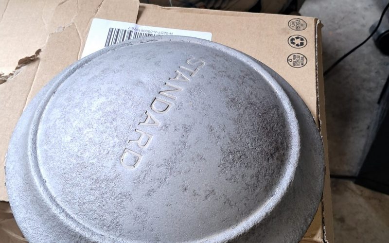 Partially restored “STANDARD” hubcap resting on a cardboard box in a workshop, with rusted parts nearby.