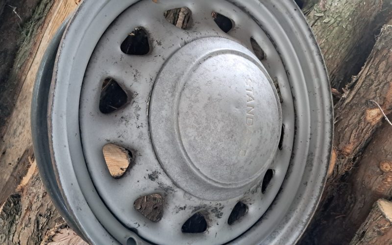 Vintage steel wheel fitted with a “STANDARD” hubcap, showing early stages of restoration with sandblasted finish.