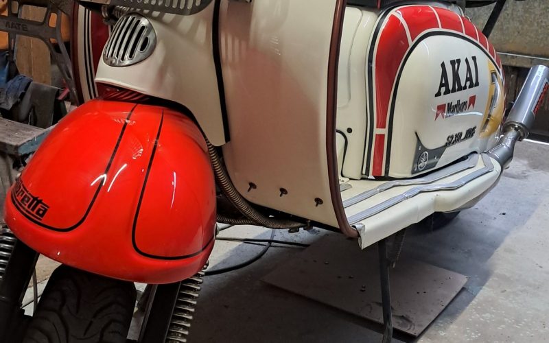 Restored Lambretta scooter with red and white AKAI livery, featuring Yamaha grill and England flag decals in a workshop.