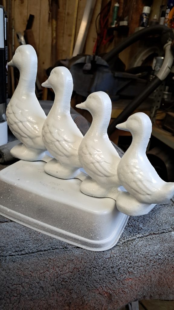 Four white duck ornaments freshly painted and drying on a workbench in a workshop.