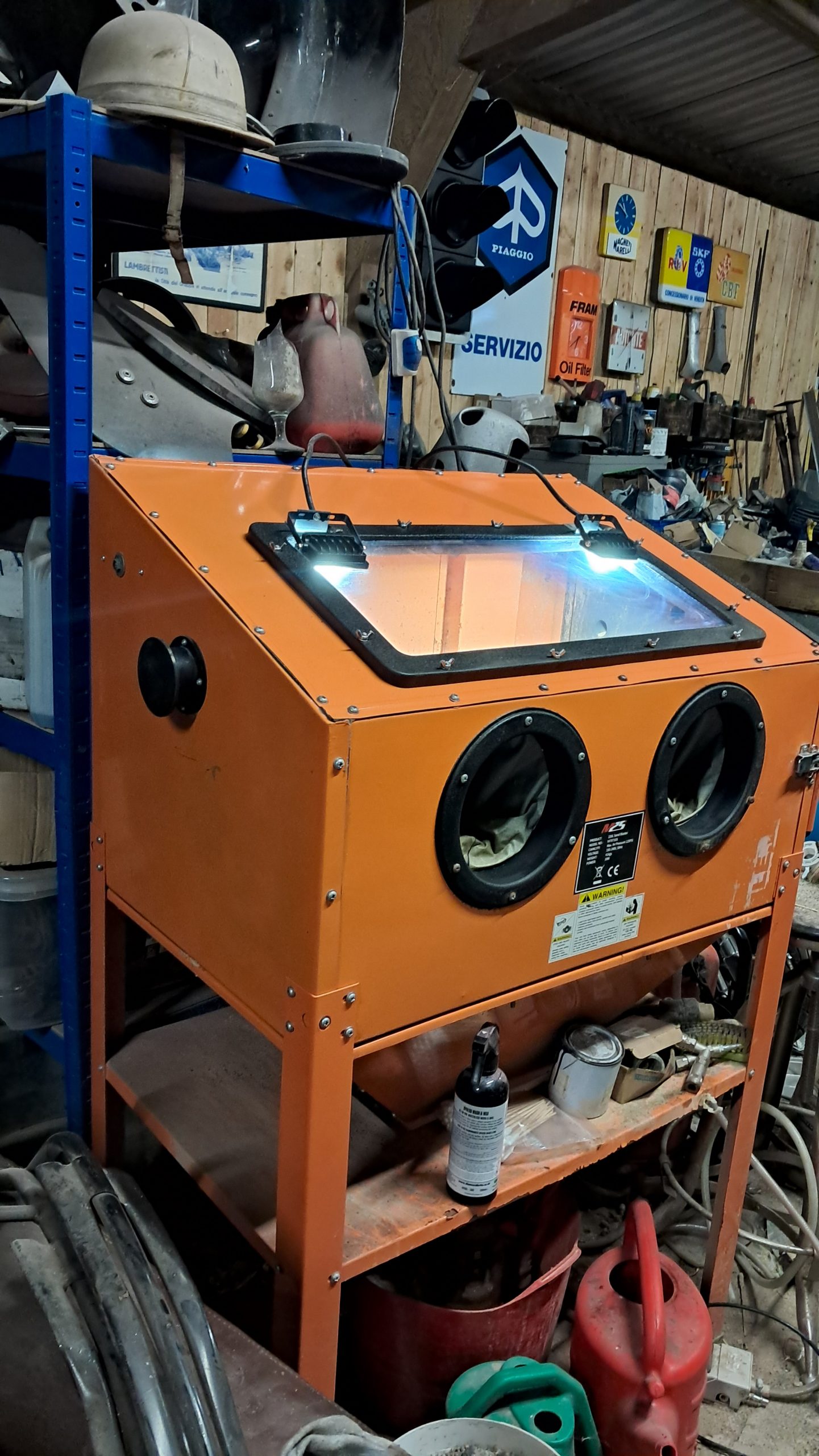 Full view of an orange blasting cabinet with gloves, inspection window and built-in LED lighting in a workshop environment.