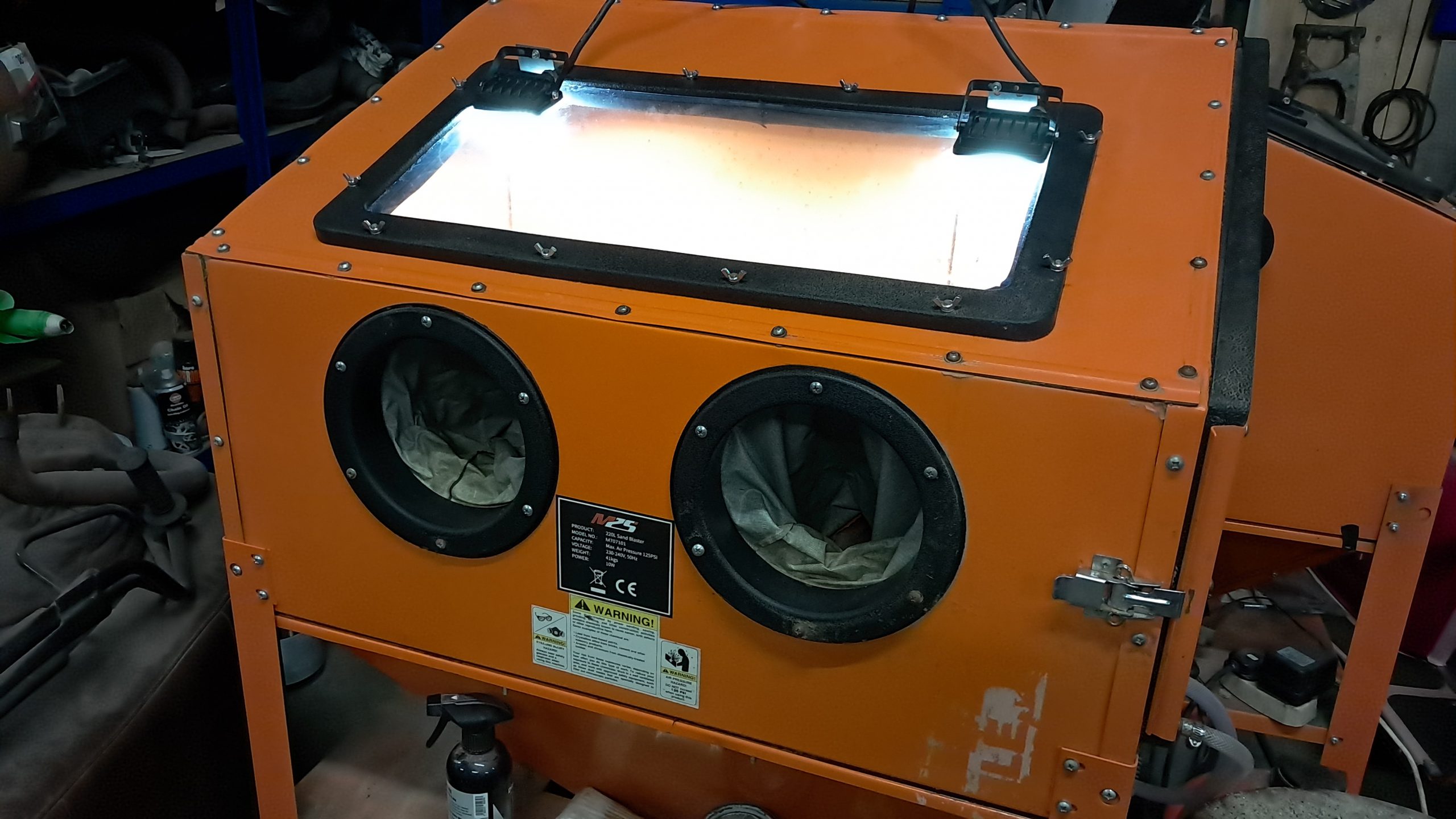 Close-up of sandblasting cabinet glass viewing panel with lighting and blasting residue visible.